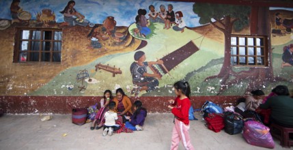 Mayan families in traditional clothes squat in front of a mural at the market in Chichicastenango,
