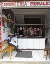 Guatemalan man wearing cowboy hat sits in a butcher shop in Chichicastenango, Highlands, El Quiché
