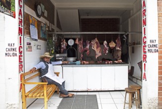 Guatemalan man wearing cowboy hat sits in a butcher shop in Chichicastenango, Highlands, El Quiché