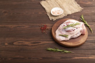 Raw Turkey Thigh with spices and rosemary on cutting board on brown wooden background and linen