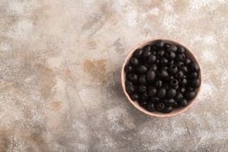 Fresh black olives in ceramic bowl on brown concrete background. Top view, flat lay, copy space