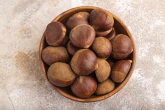 Wooden bowl with raw edible ?hestnuts on brown concrete background, top view, flat lay, close up,