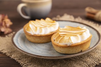 French lemon tart with meringue on brown wooden background, cup of coffee, linen textile, side
