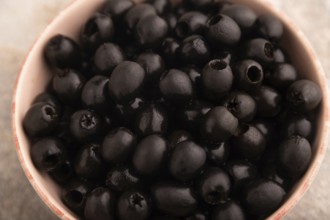 Fresh black olives in ceramic bowl on brown concrete background. side view, close up, selective