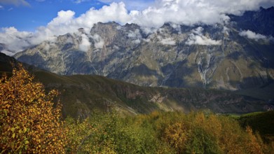 A mountainous landscape with dramatic clouds and golden autumn trees, Stepantsminda, Georgia