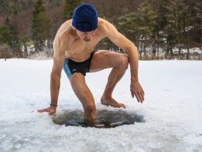Man with cap, 55, climbs into an ice hole for ice bathing, Thumsee, Bad Reichenhall,