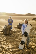 Young woman with snowboard in the sand dunes, near Merzouga, Meknès-Tafilalet region, Erg Chebbi,