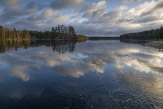 Ice and clouds reflecting on the water surface, lake in a forest, Finland