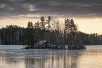 Small island with a red house, frozen lake in winter, edge of forest, near Hartola, Finland