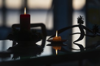 Two candles stand on a table in front of a window at dusk and create a Christmas atmosphere, plus