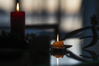 Two candles stand on a table in front of a window at dusk and create a Christmas atmosphere,