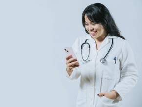 Smiling asian doctor using smartphone isolated. Young asian female doctor using phone, Female