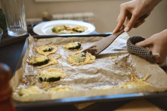 Unrecognizable woman transfers roasted smashed broccoli with cheese from baking sheet to plate