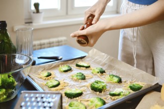 Woman sprinkles pepper over broccoli on a baking tray covered with cheese in a kitchen. The scene
