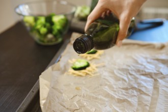 Broccoli florets and cheese are being prepared in a kitchen. Olive oil is drizzled on parchment to