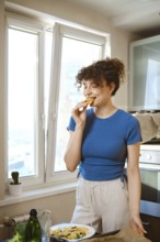 Woman bites smashed broccoli with cheese. The window opens to a city view. Fresh ingredients are on