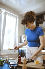 In a bright kitchen, a woman prepares smashed broccoli mixed with cheese. She stands at the
