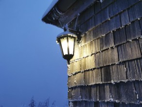 Glowing lantern on a wooden wall at a cold, blue twilight, Fichtelgebirge, Bavaria