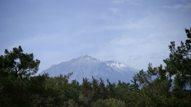 A snow-covered mountain above a wooded landscape under clear skies, view of Mount Tahtali, Lycia,