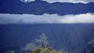 Church on a hill below a massive mountain with a band of clouds, Gergeti Monastery, Georgia