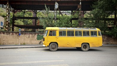 An old yellow bus is parked in front of an abandoned industrial plant in an urban area, Alaverdi,