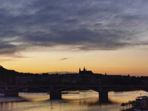 Dusk over a city with a bridge, river and silhouette of buildings in the background, Prague, Czech