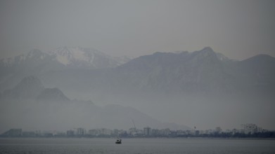 Foggy lake with a distant boat against a mountain backdrop, Antalya, Turkey