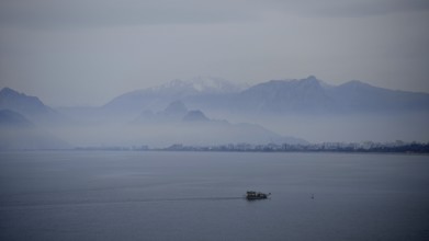 Single boat sails across foggy lake against mountain backdrop, Antalya, Turkey