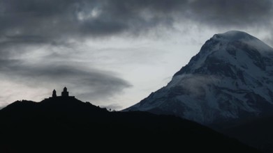 Silhouette of a church in front of a snow-covered mountain at dawn, Gergeti monastery with Kazbek