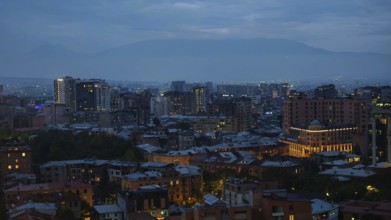 Nighttime city scene at dusk with illuminated buildings and mountains in the background, Yerevan,