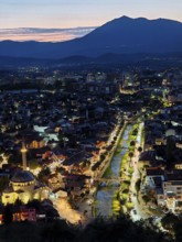 An illuminated urban panorama at night with a central river and mountain backdrop, Prizren, Kosovo