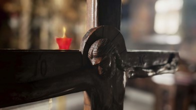 Detail of a wooden cross with a burning candle in the background in an atmospheric light, North