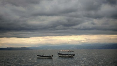 Boats on a still lake under a cloudy sky, peaceful scenery, Orhid Lake, North Macedonia