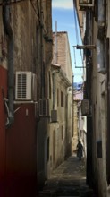Narrow, shady alley with old buildings and visible air conditioners, Koper, Slovenia