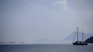A sailboat in a foggy atmosphere on the sea with silhouetted mountains, Antalya, Turkey