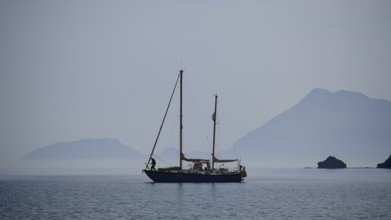 A lonely sailboat in the still sea with misty mountains in the background, Antalya, Turkey