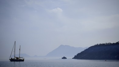A sailboat in the misty sea with silhouetted mountains in the background, Antalya, Turkey