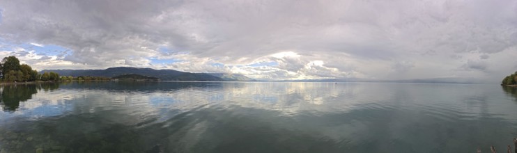 Panoramic picture of a calm lake with mountains and clouds in the background, Lake Ohrid, North