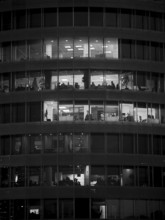 Black and white photo of an illuminated office building with visible floors and people, Tirana,