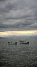Two boats calm on a lake under a thick, cloudy sky, Orhid Lake, North Macedonia