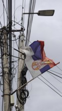 Serbian flag on a power pole blowing in the wind against a grey sky, Kosovo
