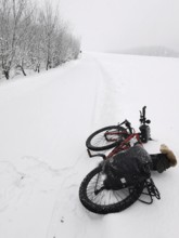Bicycle is lying in the snow on a snowy dirt road under bare trees