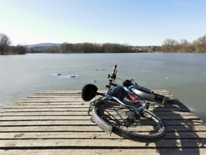A bicycle is lying on a jetty on a wintry, partly frozen lake