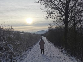 Woman walking on a snowy path at sunset through the winter landscape, Franconian Forest