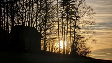 Barn and tree silhouettes against rising sun and colorful sky at dawn