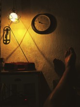 Cosy, warm scene with lamp and clock on the wall, cast shadows and a relaxed leg on the table