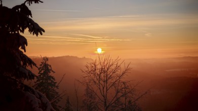 Sunrise over a misty mountain landscape with trees and a morning sky
