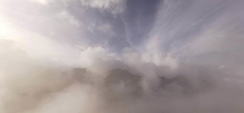 Soft cloud formations over foggy mountain peaks in mild light