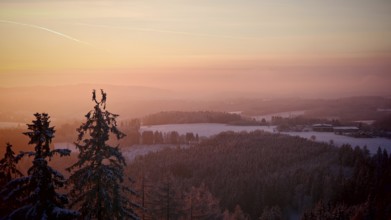 Colourful sunset over a snowy hill and forest landscape