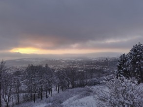 Snow-covered hills and trees under a dramatic sunset, view over Kronach in the Franconian Forest